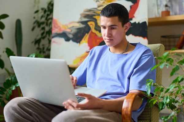 Young Man Sits in Blue T-Shirt at His Laptop